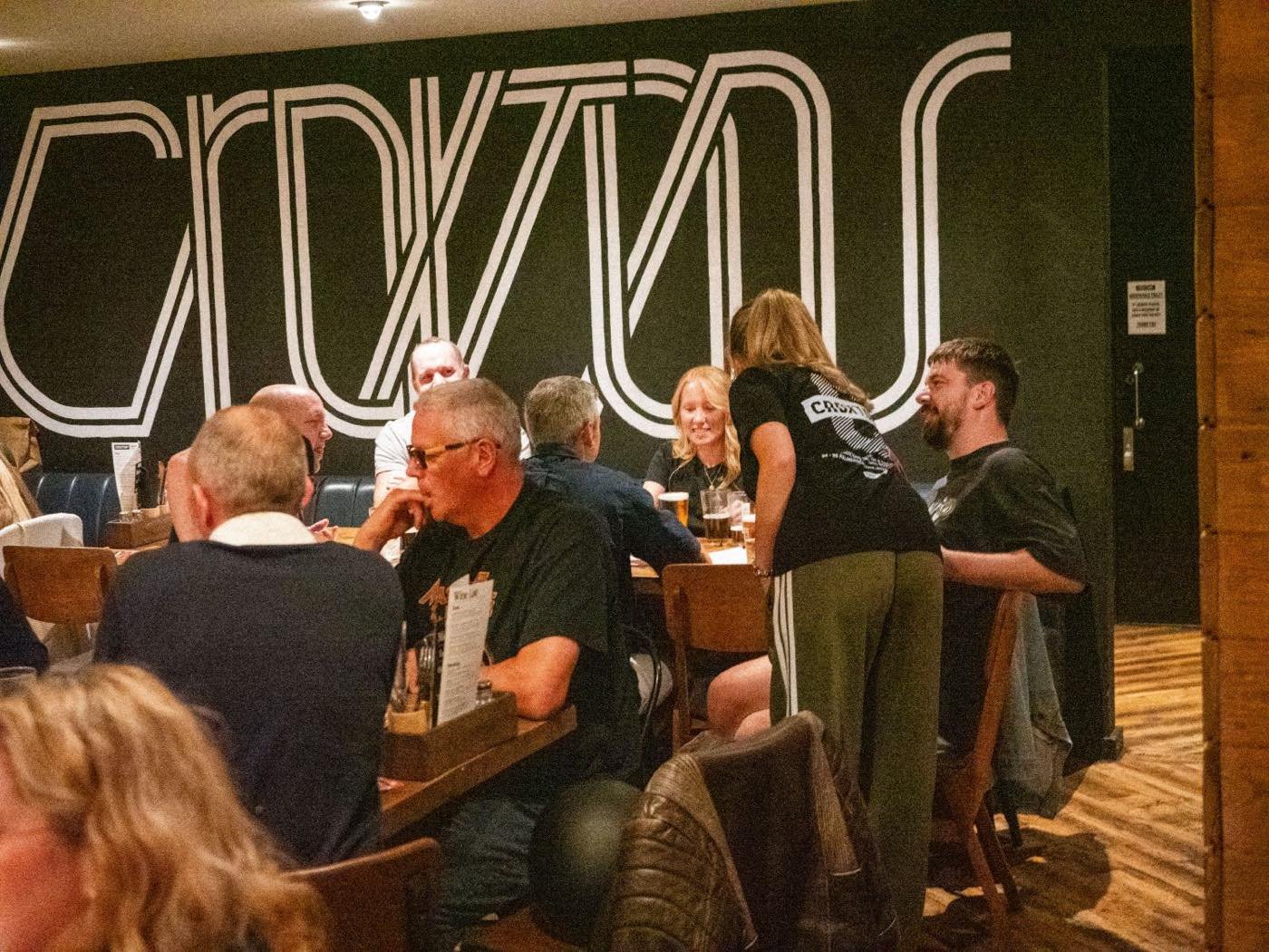 A full room at Croxtons in front of the large CROXTONS mural, staff taking orders at a busy table