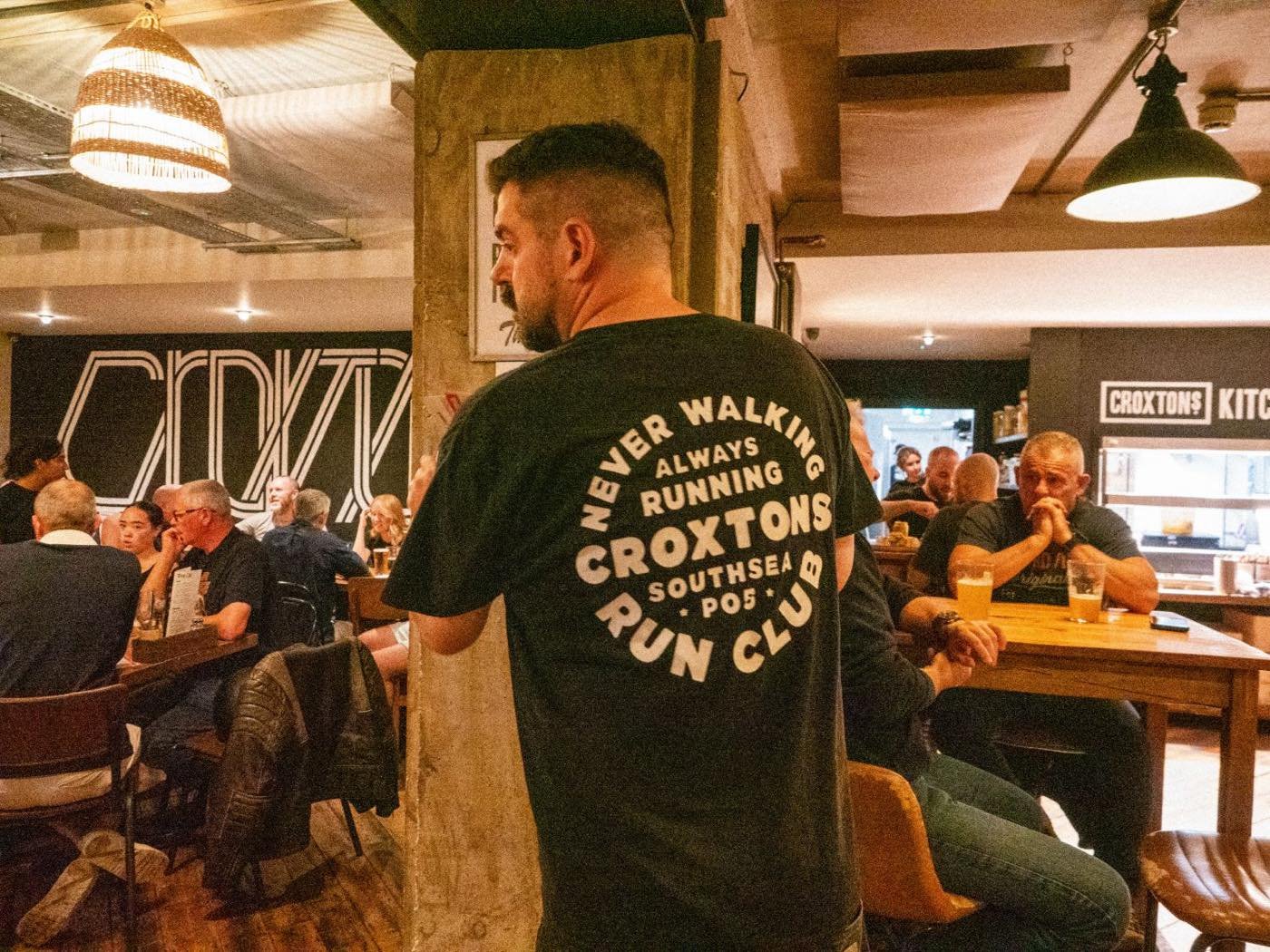 A Croxtons Run Club t-shirt reading Never Walking, Always Running, worn in the busy bar