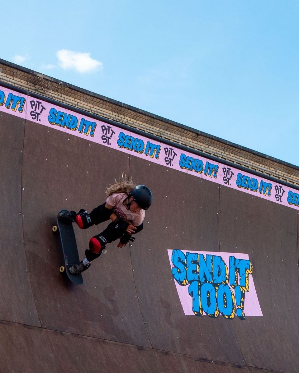 A young skater dropping in on the vert ramp beside the Send It 100 graphic